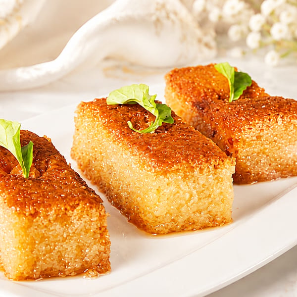 Three rectangular pieces of golden-brown semolina cake, garnished with green leaves, on a white plate.