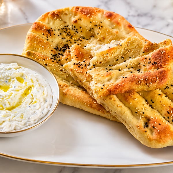 Golden flatbread with sesame seeds and a bowl of creamy dip drizzled with olive oil.