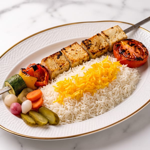 Grilled tofu and vegetable skewer with white and saffron rice, roasted tomato, and pickled vegetables.